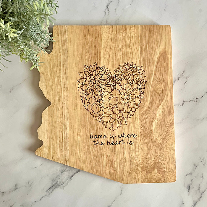 An Arizona-shaped charcuterie board with a succulent heart design and the phrase 'Home is where the heart is' engraved.