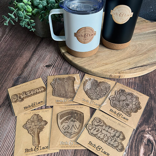 A collection of wood veneer stickers with various designs placed on a wooden surface, alongside two tumblers with wooden bases.