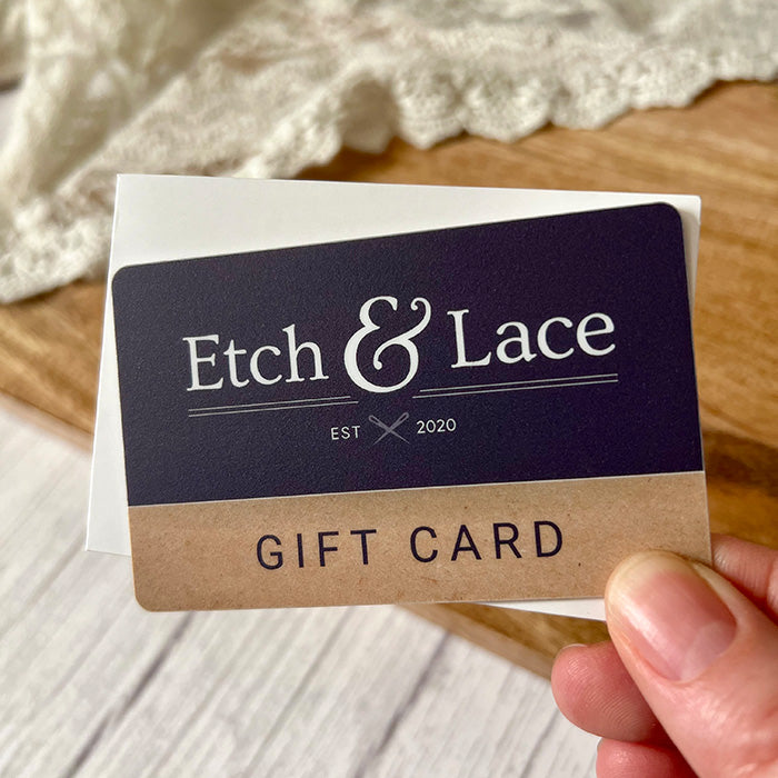 A hand holding a navy-colored gift card with 'Etch & Lace' branding and the text 'GIFT CARD'.
