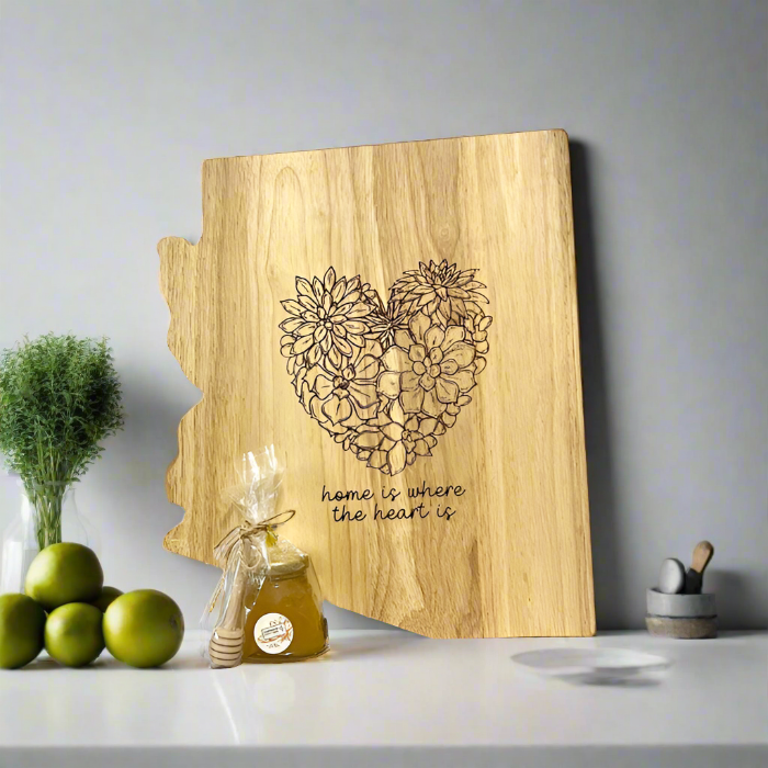 A wooden charcuterie board shaped like Arizona with a succulent heart design, accompanied by a honey set including a jar of honey and a mini honey dipper, displayed on a kitchen counter.