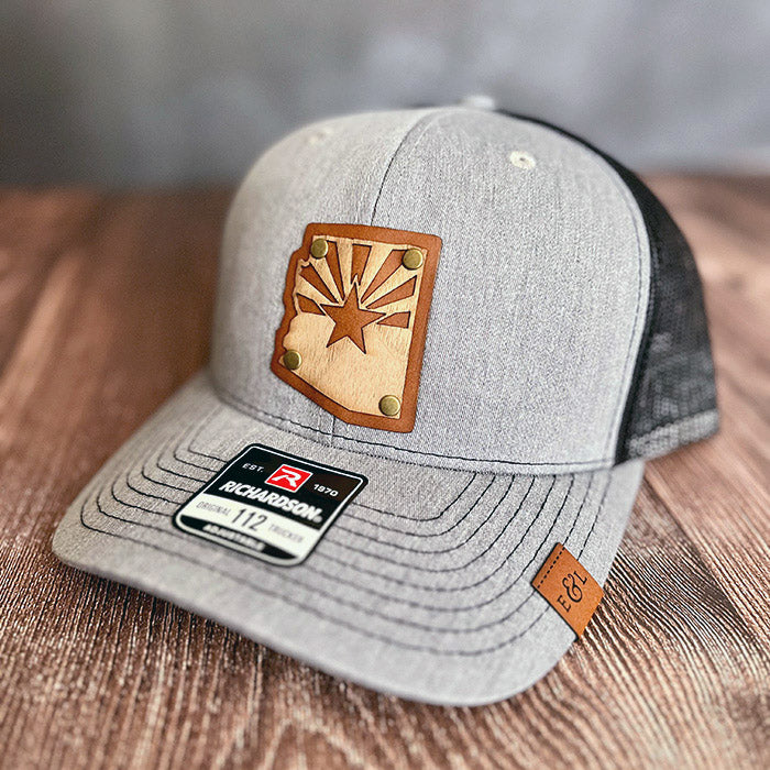 A gray trucker hat with an Arizona state flag wood veneer and leather patch on the front. Richardson 112 style is available in most options.