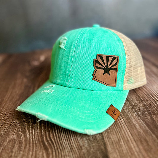 A teal ponytail hat with a laser-engraved vegan leather patch displaying the Arizona State Flag design.