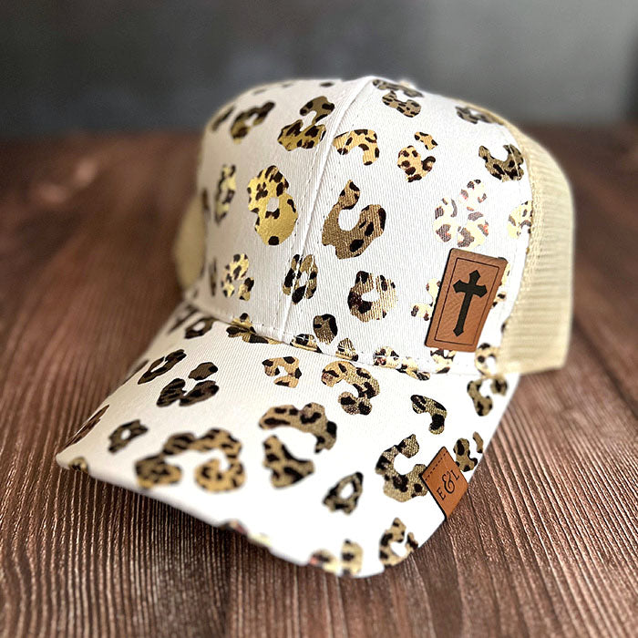 A white ponytail hat with leopard print pattern and a Christian cross-etched patch on the front.
