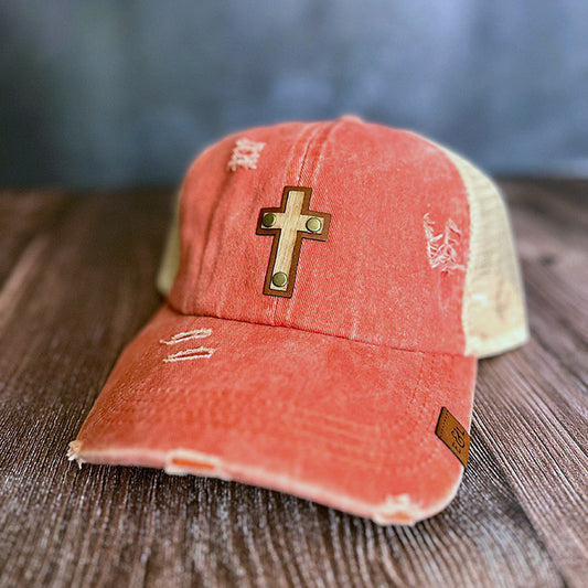 A distressed orange ponytail hat with a cross wood veneer and leather patch on the front.