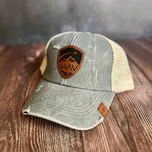 A gray and beige ponytail hat with a vegan leather patch that has 'God is Greater' design on the front.