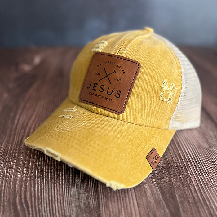 A yellow ponytail hat with a brown vegan leather patch that has 'Jesus The Only Way' written on it.