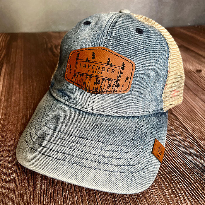 A blue denim mesh-back ponytail cap with a floral detail under the rim and a rawhide leatherette patch with a lavender fields design on the front.