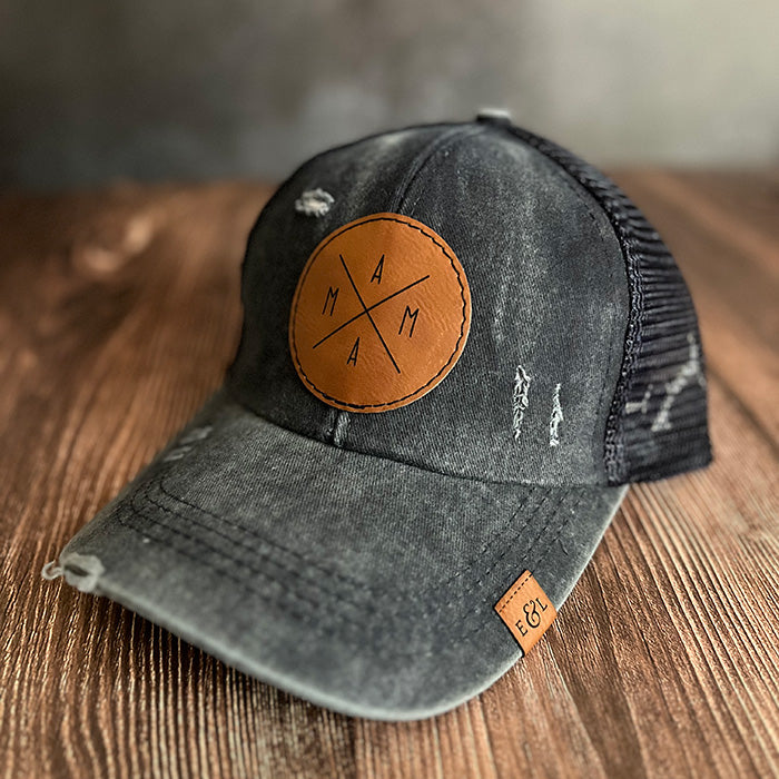 A navy distressed ponytail hat with a brown leather patch on the front that has a 'MAMA' design on it.