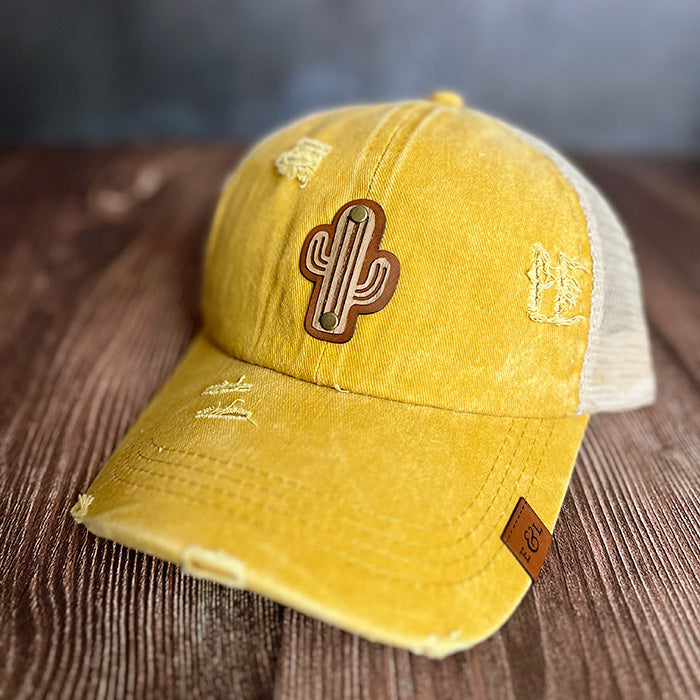 A yellow distressed ponytail hat with a saguaro wood veneer and leather patch on the front.