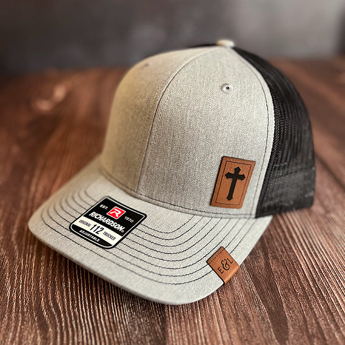A gray and black Richardson 112 trucker hat with a Christian cross-etched patch on the front.