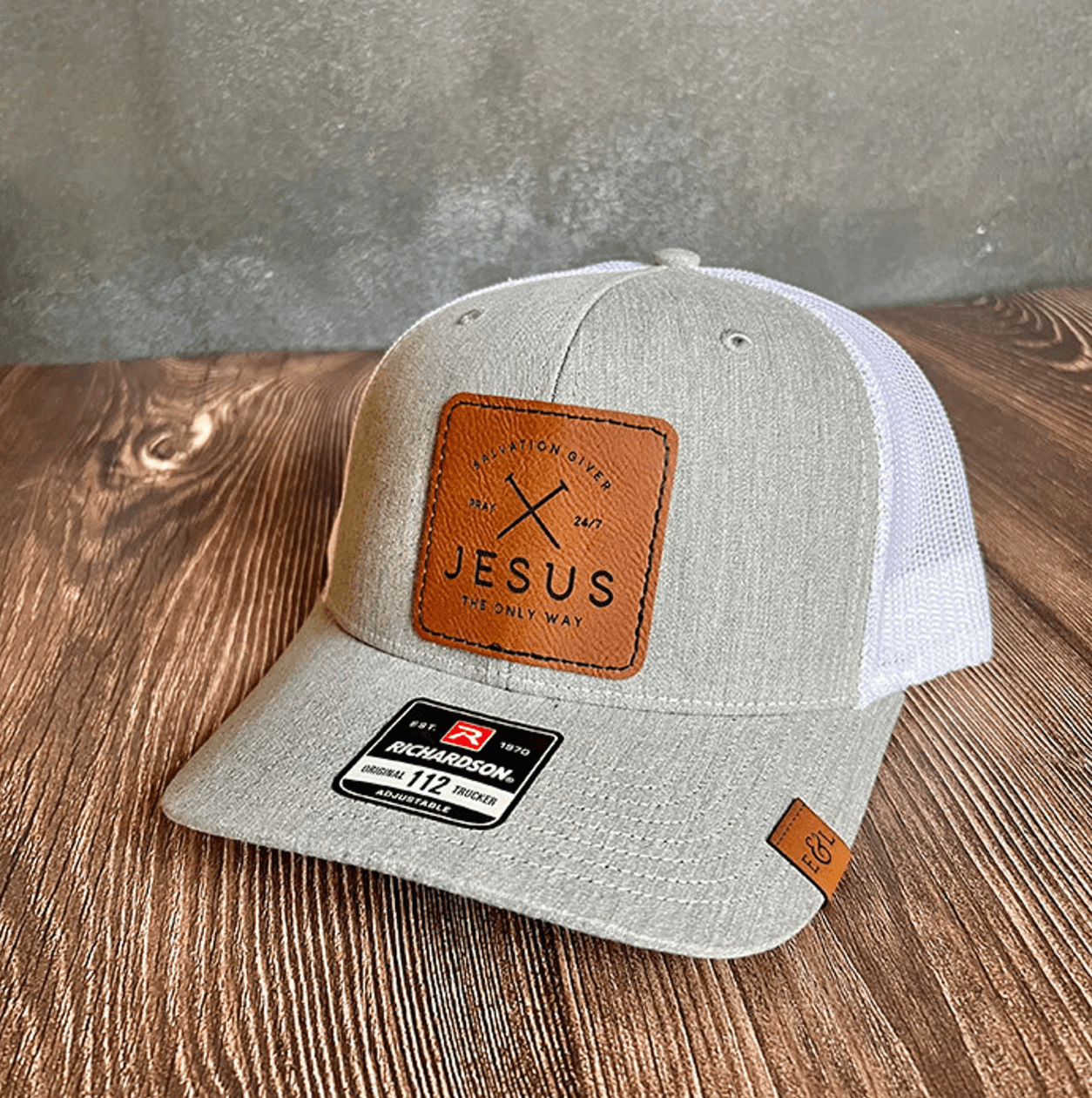 A gray Richardson 112 trucker hat with a brown leather patch on the front that has the text 'JESUS The Only Way' and Salvation Giver.