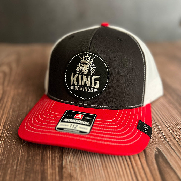 A black and red trucker hat with a vegan leather patch that reads 'King of Kings' on the front.
