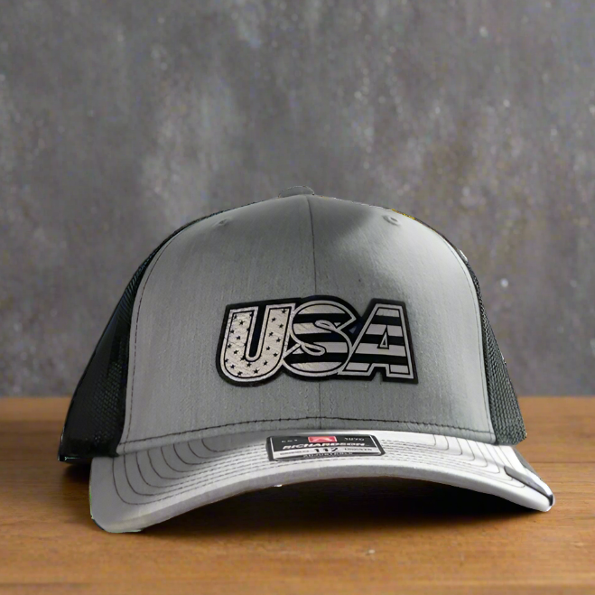 A gray and black Richardsons 112 trucker hat with a 'USA' patch on the front.