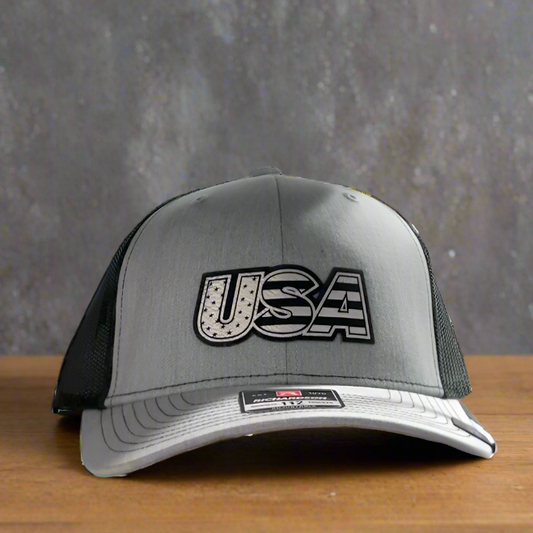 A gray and black Richardsons 112 trucker hat with a 'USA' patch on the front.