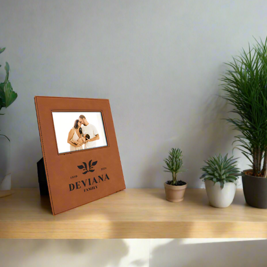 A brown leatherette picture frame with a photo of a couple displayed, placed on a wooden shelf with potted plants and decorative items around.