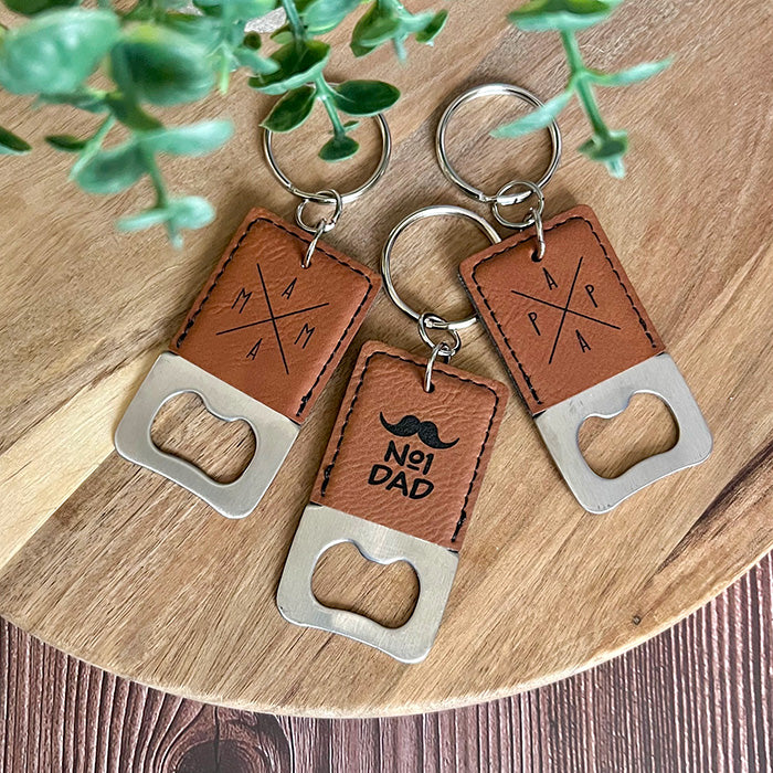 Leather keychains with bottle openers on a wooden surface with greenery.