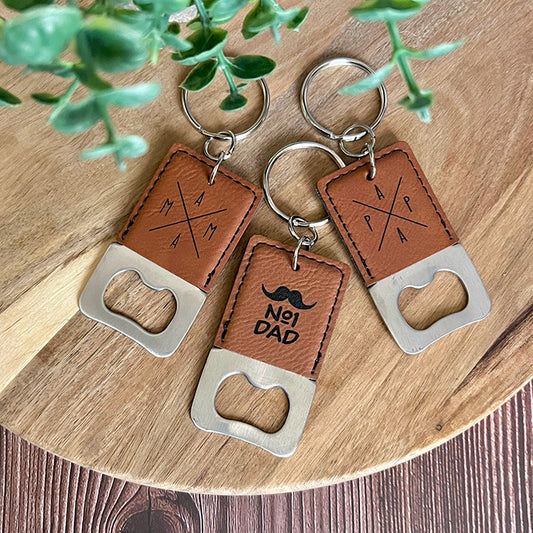 Leather keychains with bottle openers on a wooden surface with greenery.