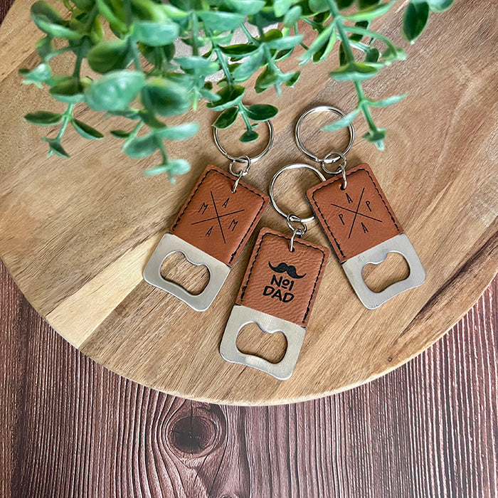Three leather bottle opener keychains on a wooden surface with a plant in the background.