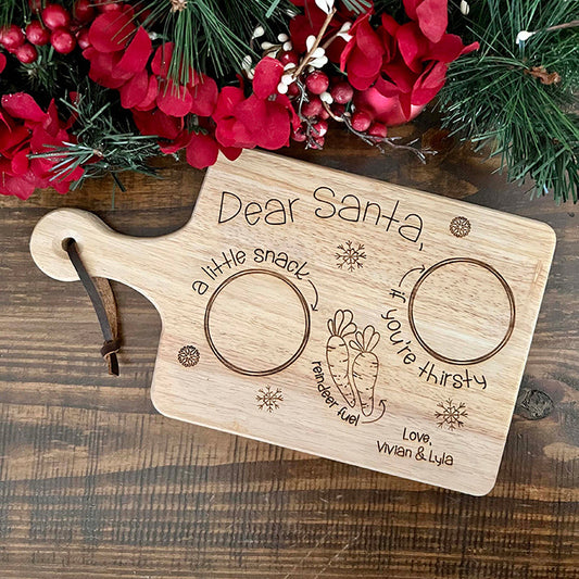 A wooden snack board with 'Dear Santa' text and holiday-themed illustrations, including carrots and snowflakes, accompanied by a genuine leather strap.