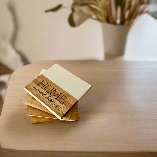 A set of four marble and wood coasters with 'Home Sweet Home' engraved on them, placed on a wooden surface.
