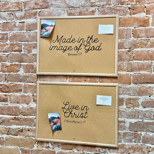 Two cork boards mounted on a wall, with one featuring an engraved scripture verse, and a photograph of a landscape with trees in the foreground.