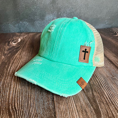 A teal ponytail hat with a Christian cross-etched patch on rawhide vegan leather.
