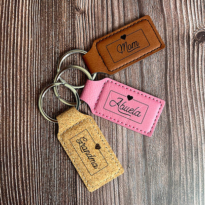 Three personalized vegan leather keychains in brown, pink, and cork, each with a different name engraved on them, displayed on a wooden surface.